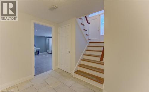 Tiled entryway featuring a staircase with wood-finish treads and white risers, a white paneled door, and an open doorway revealing a carpeted room with blue-painted walls - 106 Autumn Hill Crescent, Kitchener, ON - Indoor Photo Showing Other Room