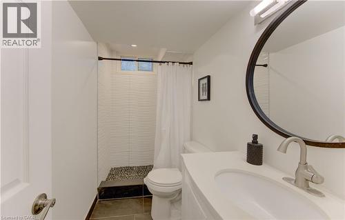 Bathroom featuring a walk-in shower with pebble tile flooring and white textured wall tile, a white vanity with an integrated sink, a brushed nickel faucet, and a round framed mirror - 106 Autumn Hill Crescent, Kitchener, ON - Indoor Photo Showing Bathroom