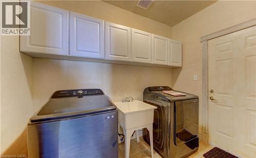 Laundry area featuring a utility sink, light-toned wall cabinets, and tile flooring - 74 Forest Edge Trail, Kitchener, ON 