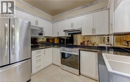 Kitchen featuring white cabinetry, dark countertops, stainless steel appliances, a mirrored backsplash, and tile flooring - 74 Forest Edge Trail, Kitchener, ON 