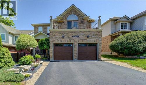 Stone facade home featuring a two-car garage with wood-finish doors, an upper-level balcony with a wrought iron railing, and an arched window - 74 Forest Edge Trail, Kitchener, ON 