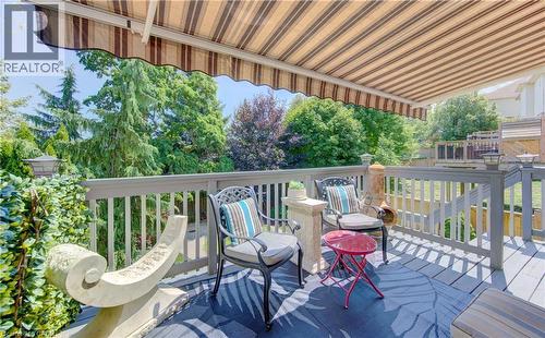 Expansive outdoor deck featuring a striped retractable awning, gray painted wood-finish decking, and a matching railing system - 74 Forest Edge Trail, Kitchener, ON 
