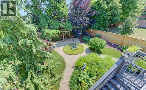 Landscaped backyard featuring a stone pathway, a central circular garden bed with a fountain, a wooden pergola, and a wooden privacy fence - 74 Forest Edge Trail, Kitchener, ON 