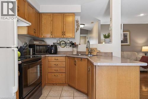 Wood-finish cabinetry with brass-tone hardware, a stainless steel faucet, and a stone-finish countertop - 10 Cadham Boulevard Unit# 29, Hamilton, ON - Indoor Photo Showing Kitchen With Double Sink