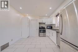 Recessed lighting illuminates the kitchen featuring white cabinetry, stainless steel appliances, and a stainless steel sink with a gooseneck faucet - 