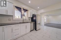 White cabinetry with stainless steel hardware, dark stone countertops, tile backsplash, stainless steel appliances, and tile flooring - 