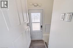 White paneled door with chrome hardware, glass-paneled entry door, wood-finish flooring, and recessed wall paneling - 