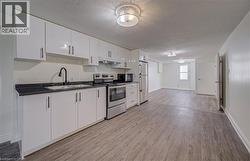 Kitchen featuring white cabinetry, dark stone-finish countertops, stainless steel appliances, and wood-finish flooring - 