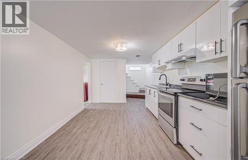 Kitchen featuring stainless steel appliances, black countertops, white cabinetry with black hardware, and wood-finish flooring - 161 Kipling Avenue, Kitchener, ON - Indoor Photo Showing Kitchen