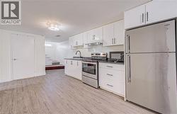 Kitchen featuring wood-finish flooring, white cabinetry, stainless steel appliances, and dark countertops - 