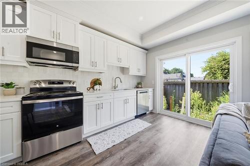 Kitchen featuring white cabinetry, stainless steel appliances, white tile backsplash, wood-finish flooring, and sliding glass doors - 11 Ontario Street, Brantford, ON - Indoor Photo Showing Kitchen