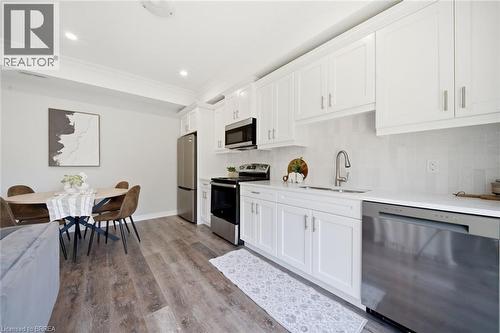 Modern kitchen and dining area featuring white shaker-style cabinetry, stainless steel appliances including a dishwasher and range, quartz countertops, a gooseneck faucet, wood-finish flooring, and re - 11 Ontario Street, Brantford, ON - Indoor Photo Showing Kitchen