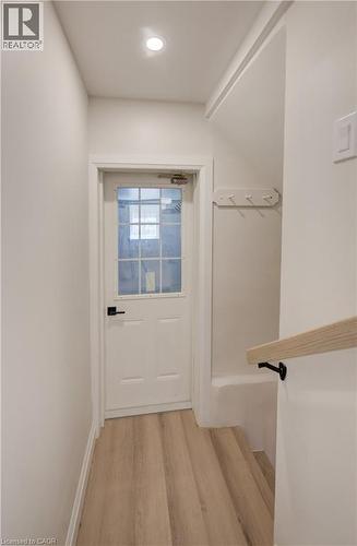 Recessed ceiling lighting, wood-finish flooring, white paneled door with window, black door hardware, and wood handrail with black brackets - 34 Moore Avenue N, Waterloo, ON - Indoor Photo Showing Other Room