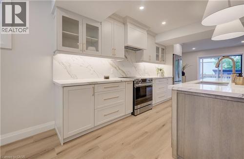 White cabinetry with glass-front accents, marble-look countertops and backsplash, stainless steel range, light wood-finish flooring, and a kitchen island with an integrated sink - 34 Moore Avenue N, Waterloo, ON - Indoor Photo Showing Kitchen With Upgraded Kitchen