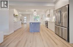 Open-concept kitchen featuring wood-finish flooring, a central island with a sink, white cabinetry, stainless steel appliances, and recessed lighting - 