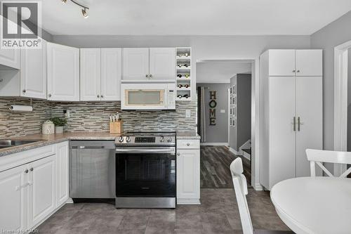 White cabinetry, stainless steel appliances, stone-finish countertops, mosaic tile backsplash, and a built-in wine rack - 60 Elford Crescent, Hamilton, ON - Indoor Photo Showing Kitchen With Upgraded Kitchen