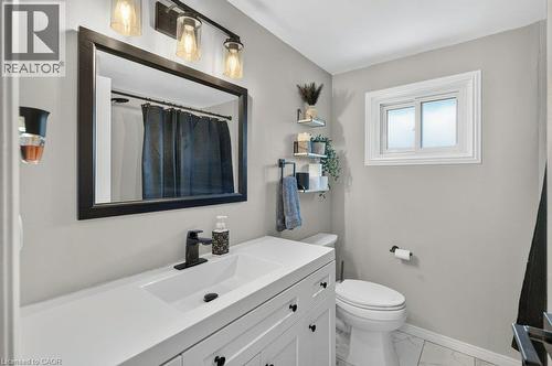 Modern bathroom featuring a white vanity with black hardware and ample countertop space, large framed mirror with integrated lighting, white subway tile surround, and a contemporary toilet - 60 Elford Crescent, Hamilton, ON - Indoor Photo Showing Bathroom