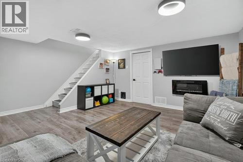 Basement living area featuring wood-finish flooring, a wall-mounted electric fireplace, a closed door, and recessed lighting fixtures - 60 Elford Crescent, Hamilton, ON - Indoor Photo Showing Living Room With Fireplace