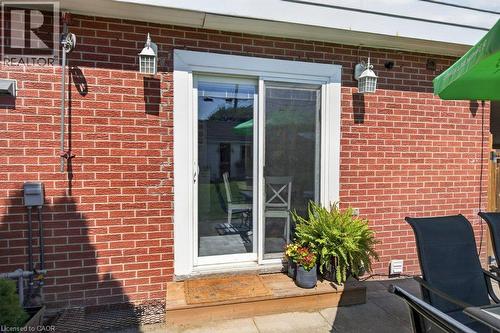 Brick exterior with a white-framed sliding glass door, dual exterior wall sconces, and a patio area - 60 Elford Crescent, Hamilton, ON - Outdoor With Exterior
