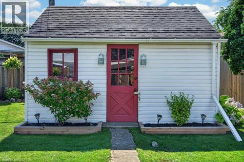 Charming cottage-style home featuring crisp white horizontal siding, a steeply pitched roof with slate-colored shingles, and a welcoming crimson entry door with multi-pane glazing - 60 Elford Crescent, Hamilton, ON - Outdoor With Exterior