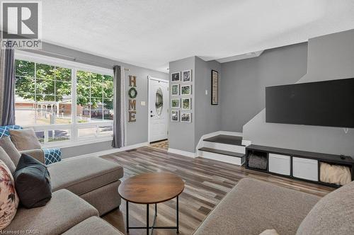 Spacious living area featuring wood-finish flooring, a large multi-pane window, and a white front entry door with an oval glass insert - 60 Elford Crescent, Hamilton, ON - Indoor Photo Showing Living Room