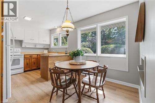 Bright kitchen and dining area featuring white cabinetry, wood-finish flooring, and large multi-pane windows flooding the space with natural light - 974 Unsworth Avenue, Burlington, ON 