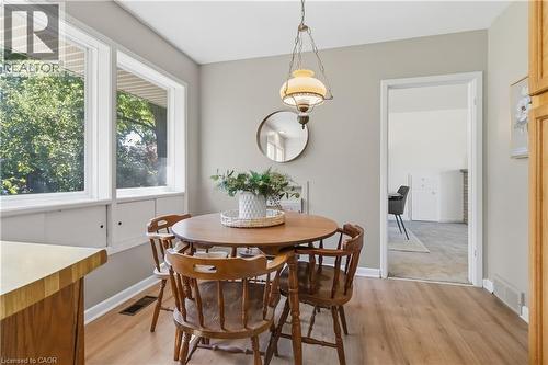 Elegant dining area featuring a round wood table with four spindle-back chairs, hardwood flooring, and abundant natural light from large casement windows - 974 Unsworth Avenue, Burlington, ON 