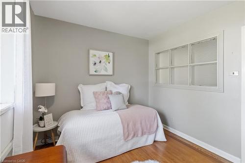 Comfortable bedroom showcasing soft pink and white bedding, a white upholstered headboard, hardwood flooring, gray walls, and a large multi-pane window - 974 Unsworth Avenue, Burlington, ON 