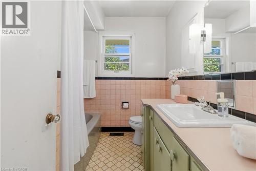 Charming bathroom featuring vintage pink tile walls, black and white tile accents, and a wood-finish vanity with integrated sink - 974 Unsworth Avenue, Burlington, ON 