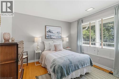 Serene bedroom retreat featuring warm wood-finish flooring, soft neutral wall palette, and abundant natural light from multi-pane glass doors with plantation shutters - 974 Unsworth Avenue, Burlington, ON 
