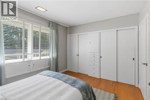 Bright, light-filled bedroom featuring hardwood flooring, expansive built-in cabinetry with multiple drawers and storage solutions, and large multi-panel windows with motorized blinds and sheer draper - 974 Unsworth Avenue, Burlington, ON 