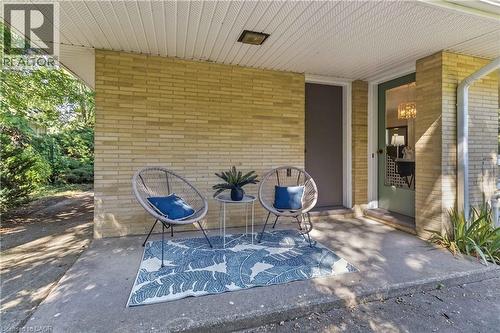 Covered front porch featuring yellow brick construction, recessed lighting, and a blue patterned outdoor rug anchoring two woven lounge chairs and a side table - 974 Unsworth Avenue, Burlington, ON 