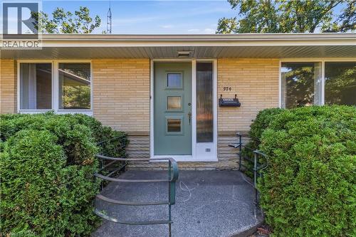 Welcoming front entrance featuring a soft sage-green entry door with multi-panel glazing, natural wood-finish siding, and a covered porch with metal railings - 974 Unsworth Avenue, Burlington, ON 