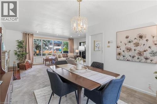Open-concept dining and living area featuring a wood-finish dining table with seating for four, black upholstered chairs, and a crystal pendant light fixture - 974 Unsworth Avenue, Burlington, ON 