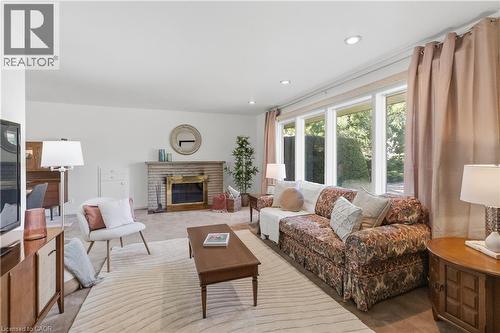 Spacious living area featuring a brick fireplace with a brass firebox, expansive windows, recessed ceiling lights, and light-toned carpet flooring - 974 Unsworth Avenue, Burlington, ON 
