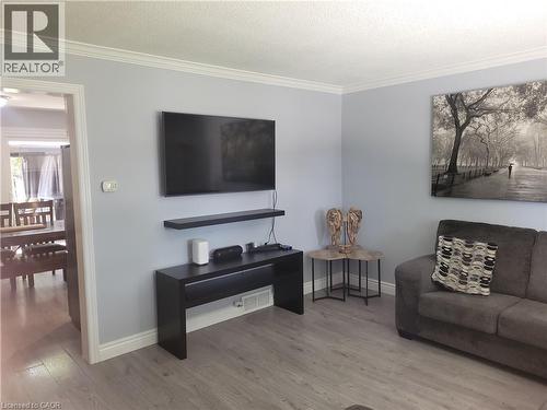 Modern living space featuring a wall-mounted flat-screen television with integrated soundbar, sleek black entertainment console with open shelving, and wood-finish flooring throughout - 23 Bentley Place, Hamilton, ON - Indoor Photo Showing Other Room