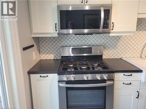 Modern kitchen featuring stainless steel gas range with six burners and convection oven, under-cabinet microwave with stainless steel finish, black quartz countertops, white cabinetry with hardware ac - 23 Bentley Place, Hamilton, ON - Indoor Photo Showing Kitchen