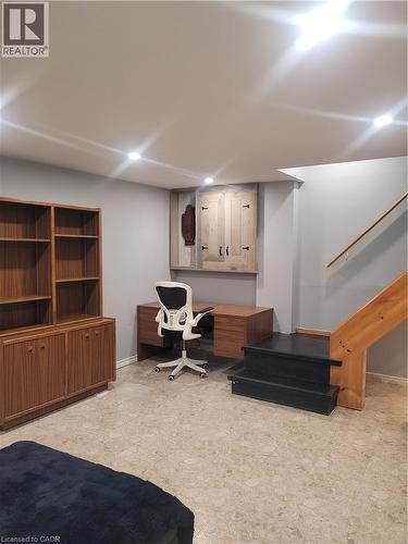 Finished basement featuring built-in wood cabinetry with glass-front shelving, recessed ceiling lighting, engineered wood flooring, and a white ergonomic office chair at a wood desk - 23 Bentley Place, Hamilton, ON - Indoor