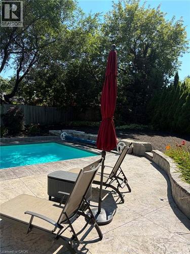 Backyard oasis featuring an in-ground swimming pool, stamped concrete patio, and a curved stone retaining wall - 23 Bentley Place, Hamilton, ON - Outdoor With In Ground Pool With Backyard