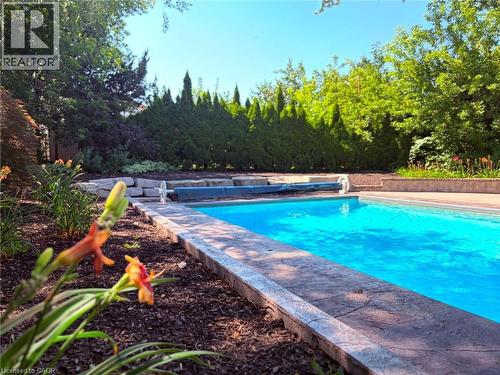 In-ground swimming pool featuring a patterned concrete surround and lush perimeter landscaping - 23 Bentley Place, Hamilton, ON - Outdoor With In Ground Pool With Backyard