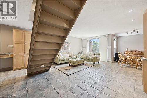 Open-concept living space featuring large format tile flooring, a built-in wooden cabinet with desk, and a prominent staircase - 36 Hayhurst Road Unit# 329, Brantford, ON - Indoor