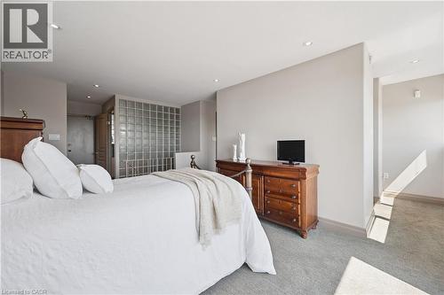 Spacious primary bedroom featuring a wood-finish dresser with drawers, recessed ceiling lighting, and an ensuite bathroom with glass block partition - 36 Hayhurst Road Unit# 329, Brantford, ON - Indoor Photo Showing Bedroom