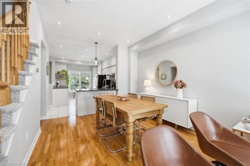 Open-concept dining and kitchen area featuring warm wood-finish flooring throughout, a solid wood dining table with seating for six, white cabinetry with integrated appliances, pendant lighting, reces - 678 Rowley Common, Burlington, ON - Indoor Photo Showing Other Room