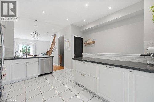 Modern kitchen featuring white cabinetry, dark countertops, a stainless steel dishwasher, and tile flooring - 678 Rowley Common, Burlington, ON - Indoor Photo Showing Kitchen