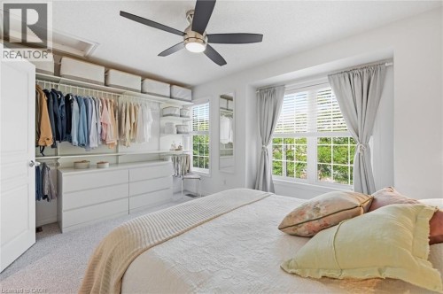 Room featuring a built-in closet system with multiple rods and shelving, a six-drawer dresser, a ceiling fan with integrated lighting, and dual windows - 678 Rowley Common, Burlington, ON - Indoor Photo Showing Bedroom