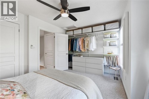 Bedroom featuring a black and brushed nickel ceiling fan, light gray carpet, white walls, and a custom closet system with white shelving, hanging rods, and integrated drawers - 678 Rowley Common, Burlington, ON - Indoor Photo Showing Bedroom