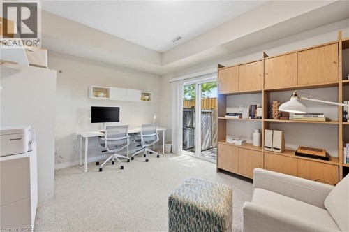 Light-toned room featuring a built-in wood-finish shelving unit, neutral carpet flooring, and a sliding glass door providing exterior access - 678 Rowley Common, Burlington, ON - Indoor Photo Showing Other Room