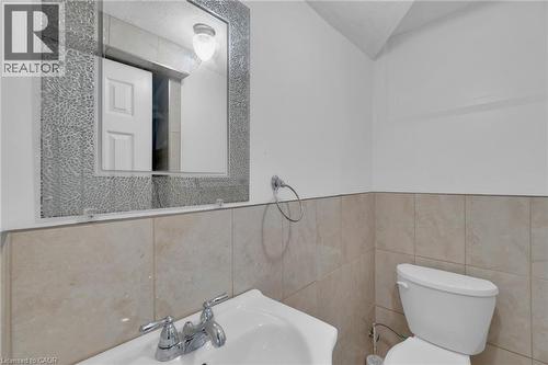 Bathroom featuring a decorative-framed mirror, wall-mounted light fixture, pedestal sink with chrome faucet, and tiled wainscoting - 197 Troy Street, Mississauga, ON - Indoor Photo Showing Bathroom