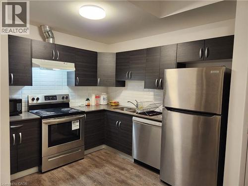 Kitchen with tasteful backsplash, appliances with stainless steel finishes, a sink, wood finished floors, and under cabinet range hood - 269 Sunview Street Unit# 607, Waterloo, ON - Indoor Photo Showing Kitchen With Stainless Steel Kitchen With Double Sink
