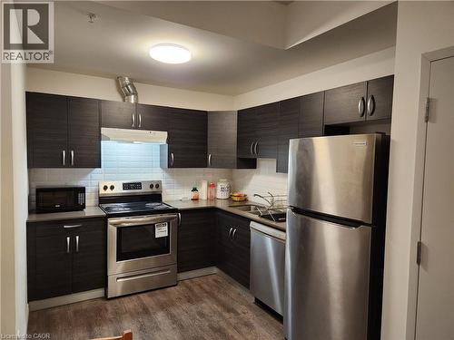 Kitchen featuring tasteful backsplash, appliances with stainless steel finishes, dark wood-type flooring, a sink, and under cabinet range hood - 269 Sunview Street Unit# 607, Waterloo, ON - Indoor Photo Showing Kitchen With Stainless Steel Kitchen With Double Sink